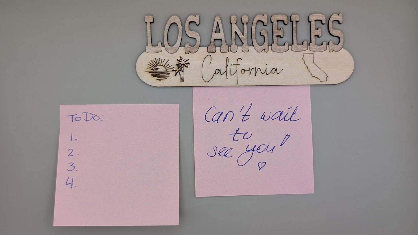 Two pink sticky notes on a gray wall with 'Los Angeles California' sign above.