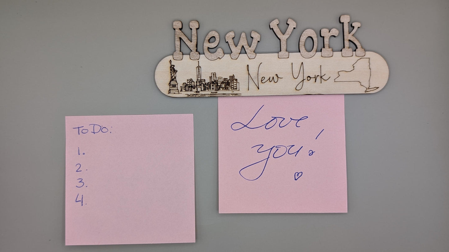 Decorative sign with 'New York' and a silhouette of the Statue of Liberty, two pink sticky notes on a gray wall.