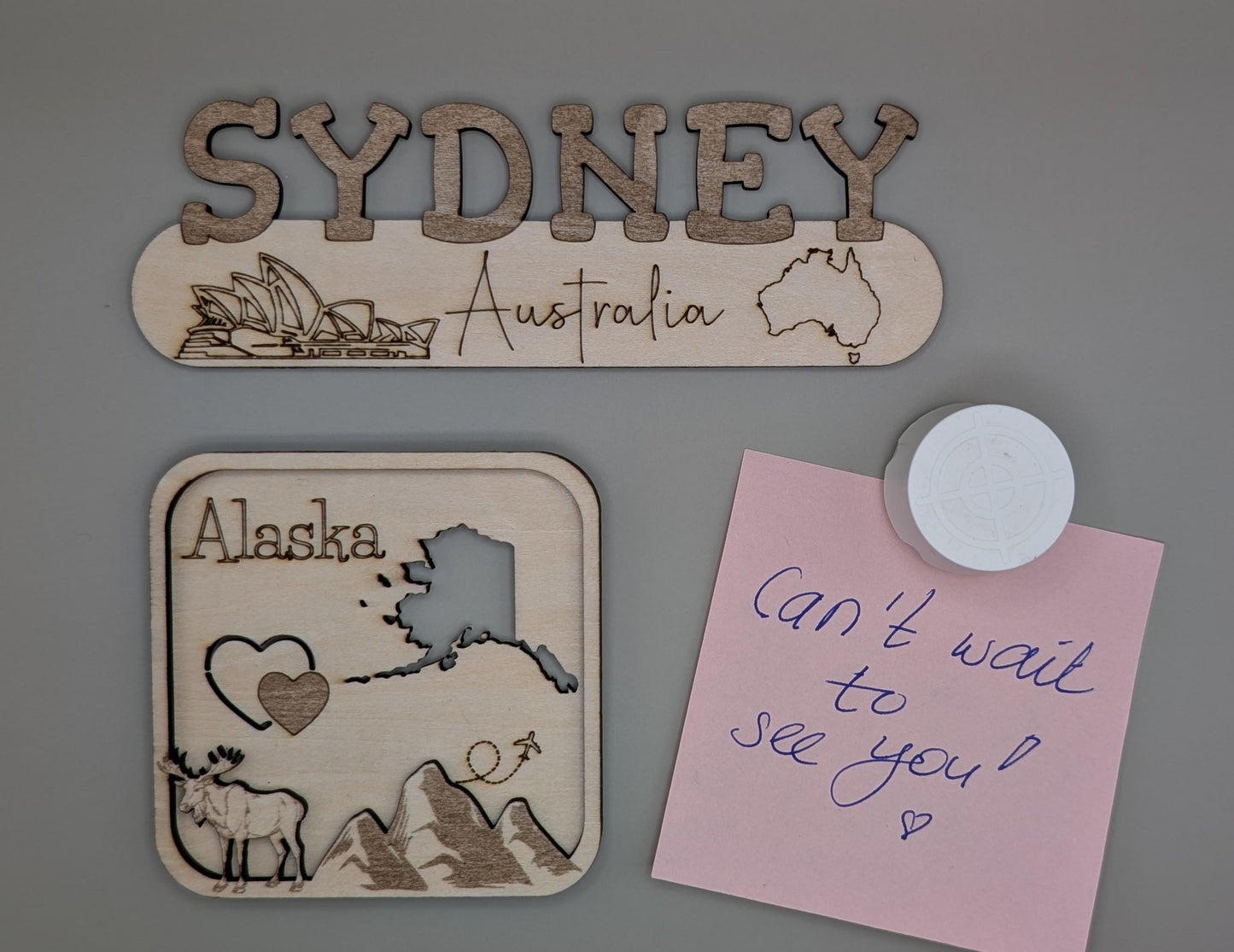 Wooden signs with 'Sydney, Australia' and 'Alaska' designs on a gray background.