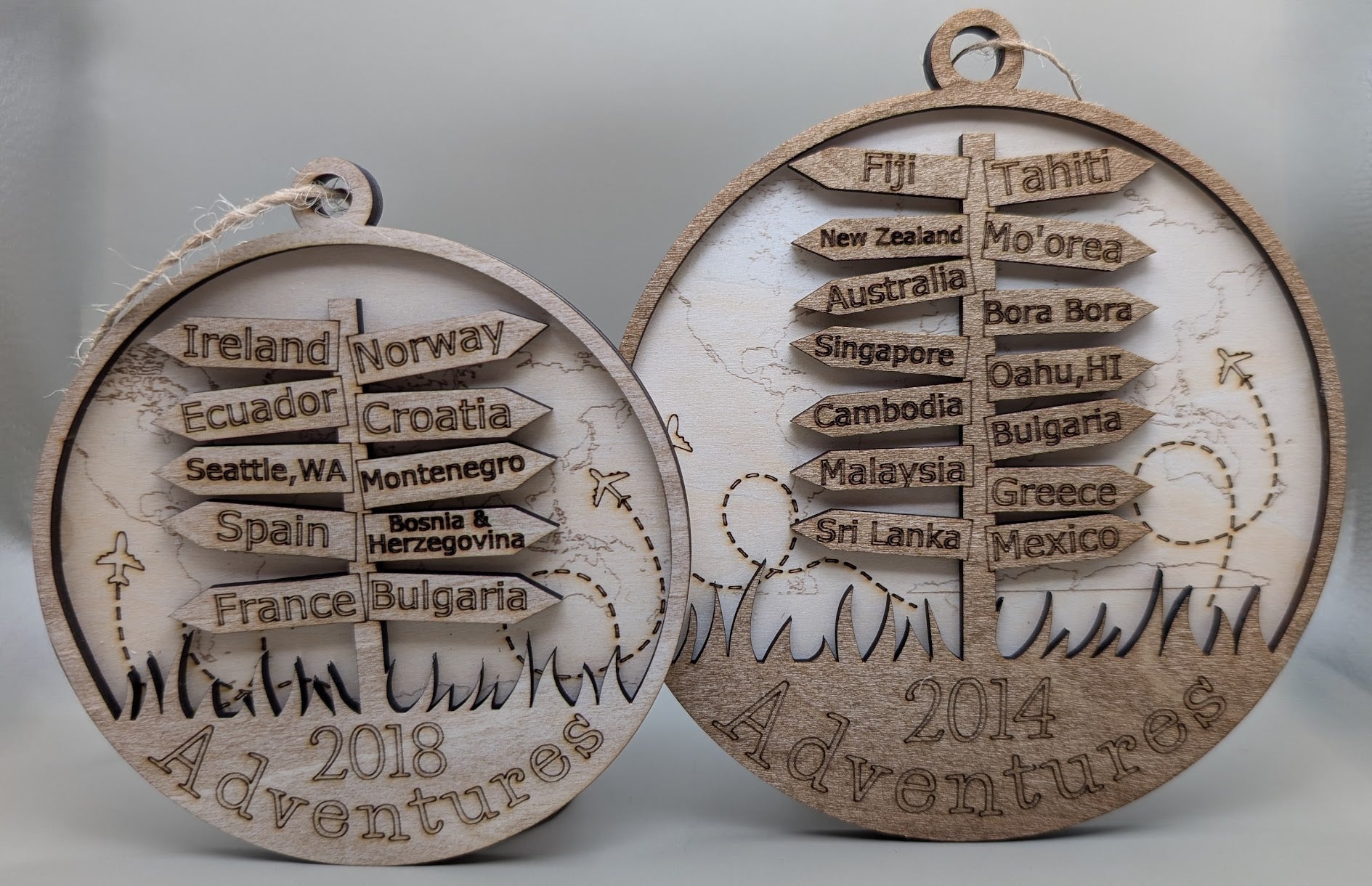 Two wooden ornaments with engraved travel destinations on a gray background.