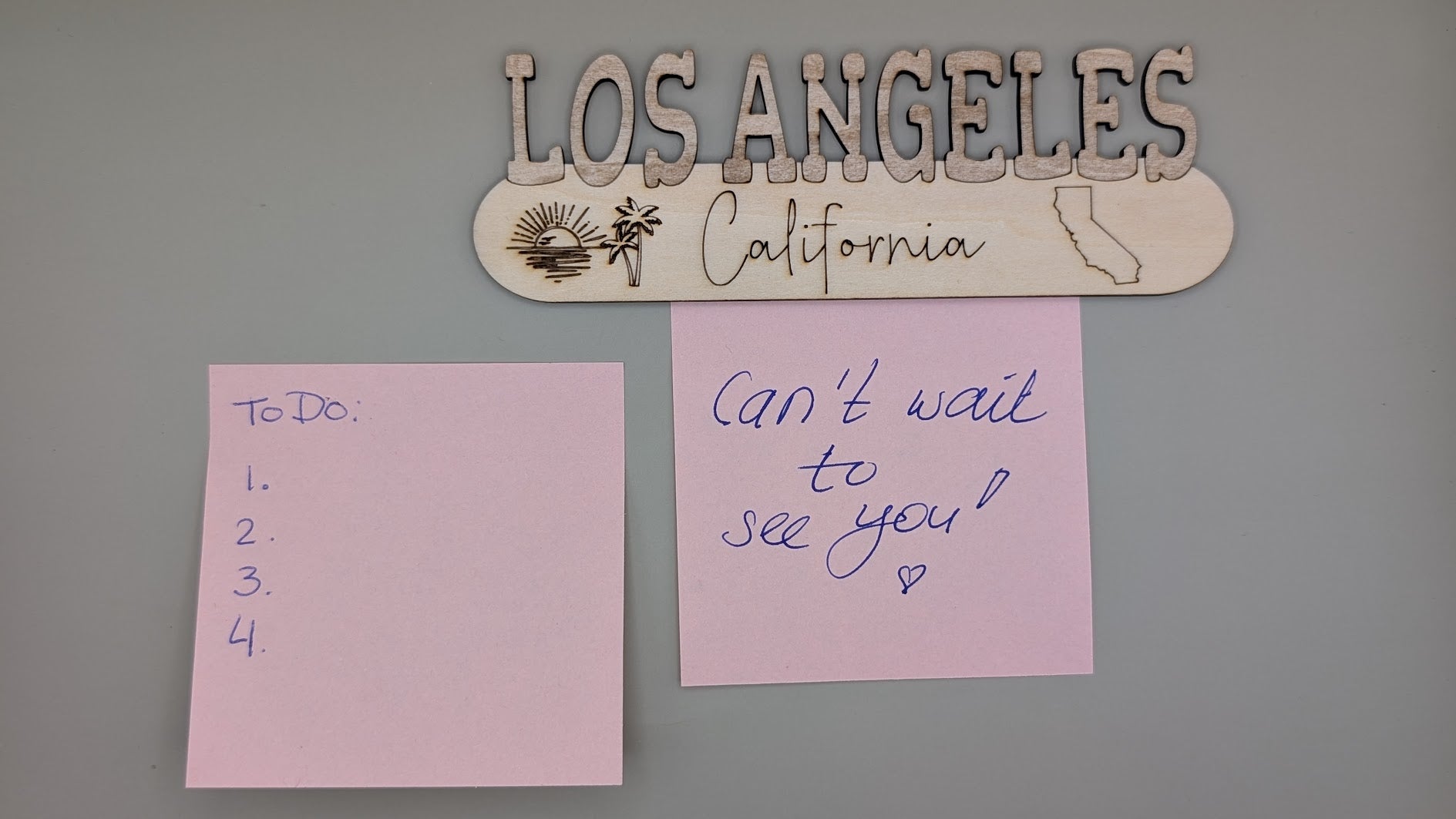 Two pink sticky notes on a gray wall with 'Los Angeles California' sign above.