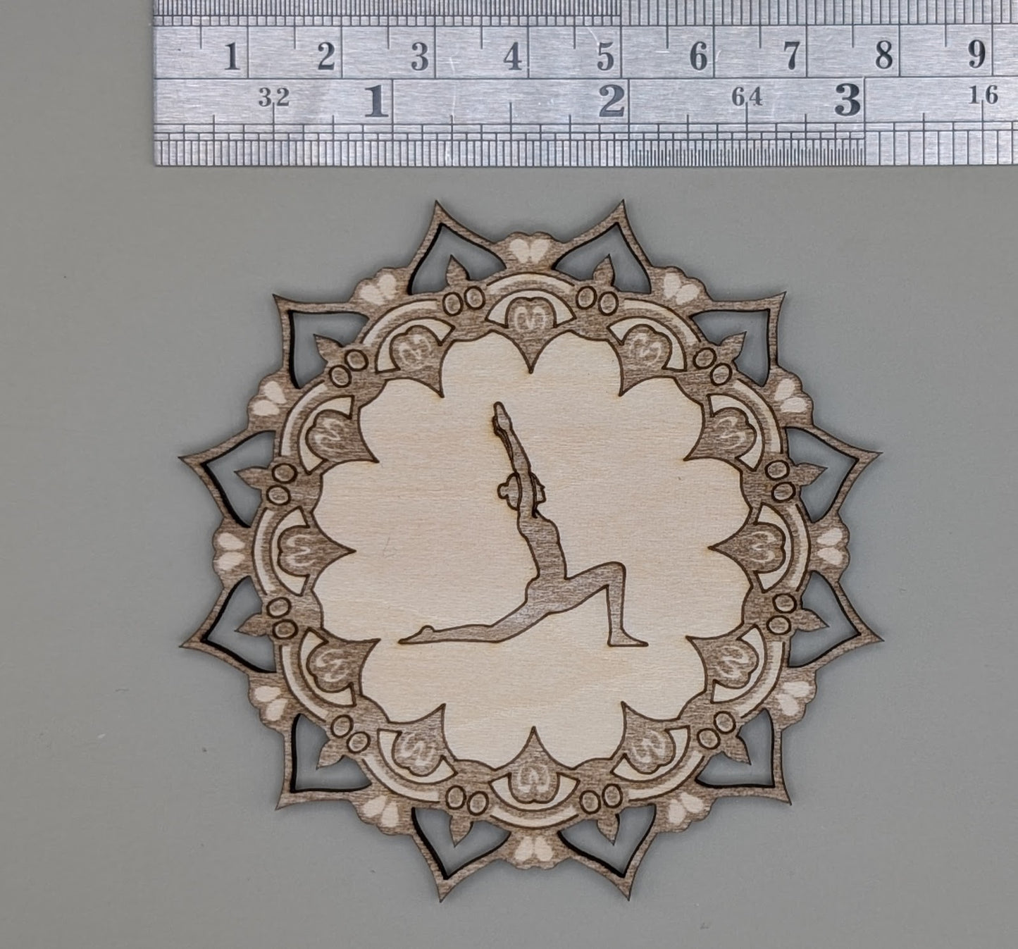 Decorative cutout with a silhouette of a person in a yoga pose, surrounded by intricate patterns, on a gray background with a ruler for scale.