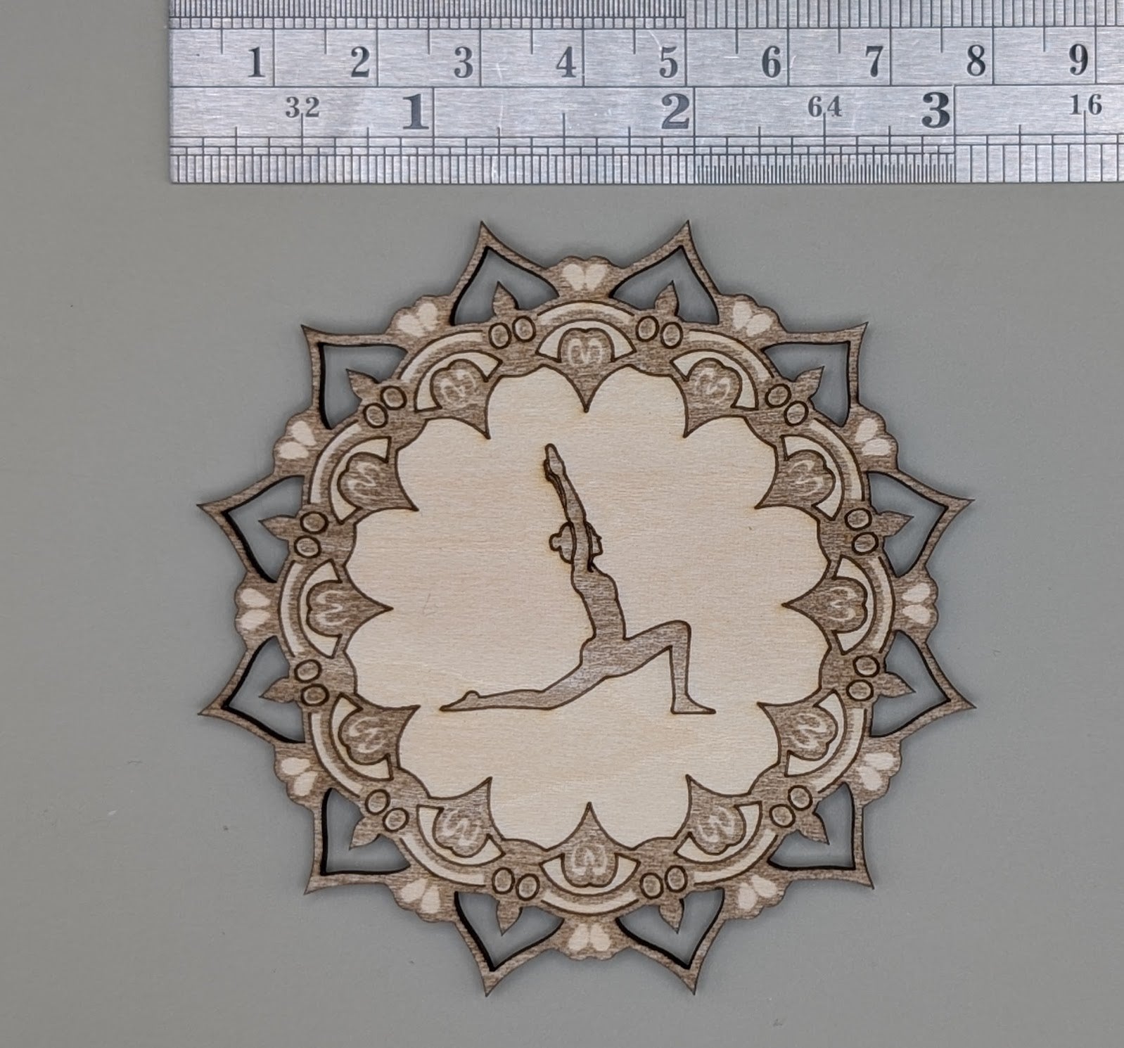 Decorative cutout with a silhouette of a person in a yoga pose, surrounded by intricate patterns, on a gray background with a ruler for scale.