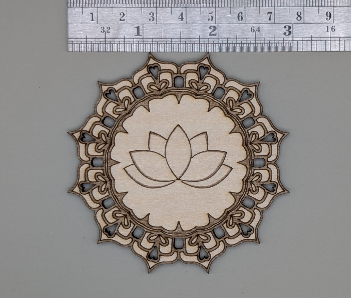 Decorative wooden cutout with lotus flower design on a gray surface with a ruler for scale.