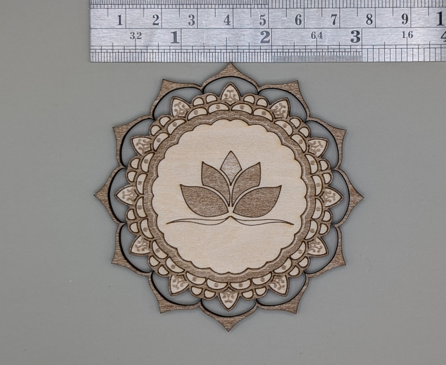 Decorative cutout with leaf design and mandala pattern on a gray background, measured against a ruler.