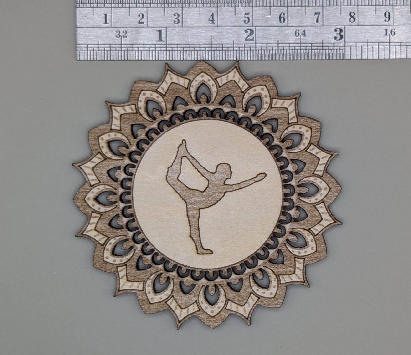 Decorative wooden cutout with a dancer silhouette inside a mandala design, measured against a ruler.
