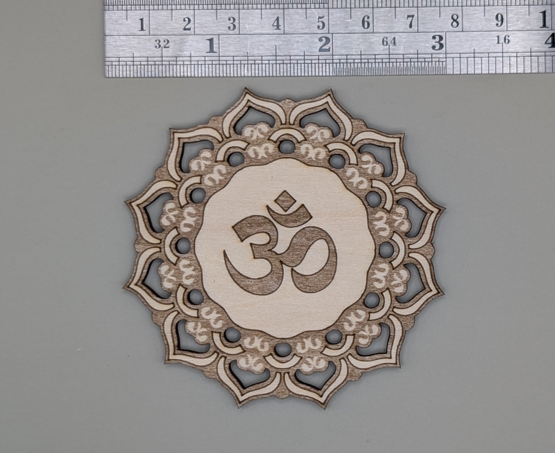Decorative wooden cutout with Om symbol and mandala design, measured against a ruler.