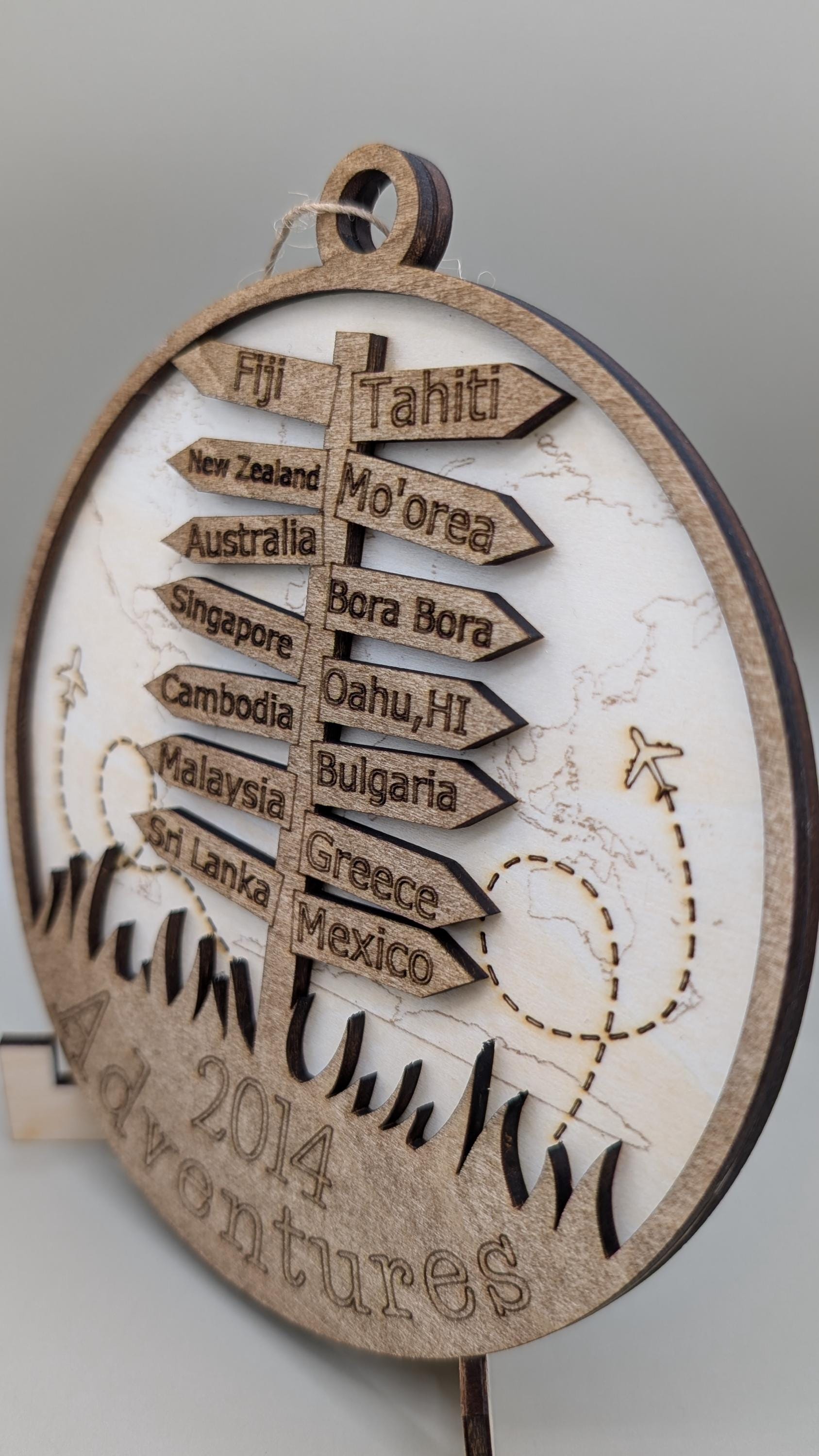 Wooden plaque with laser-cut cutout of a signpost with travel destinations and '2014 Adventures' text.