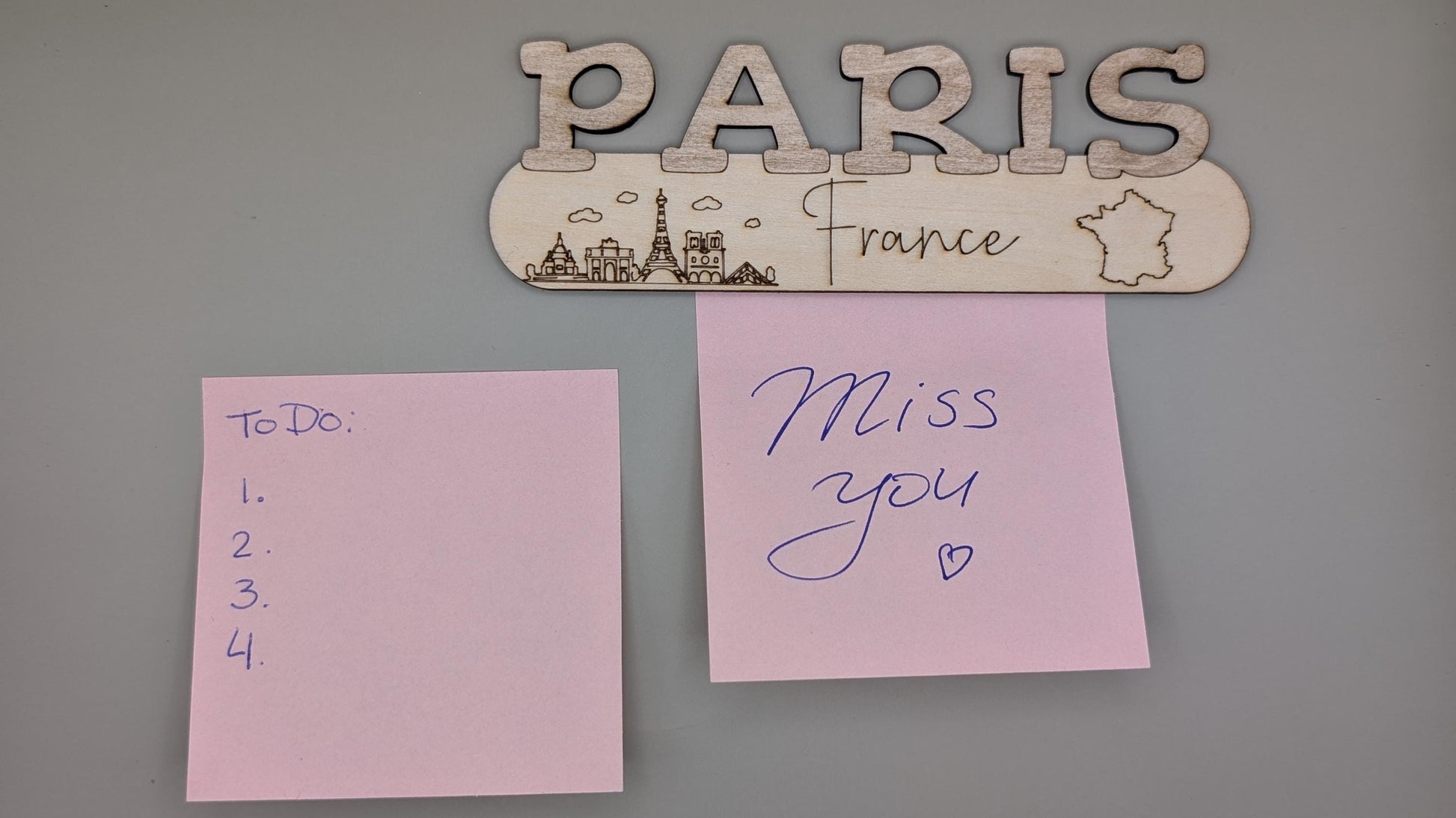 Decorative sign with 'PARIS France' above two pink sticky notes on a gray background.