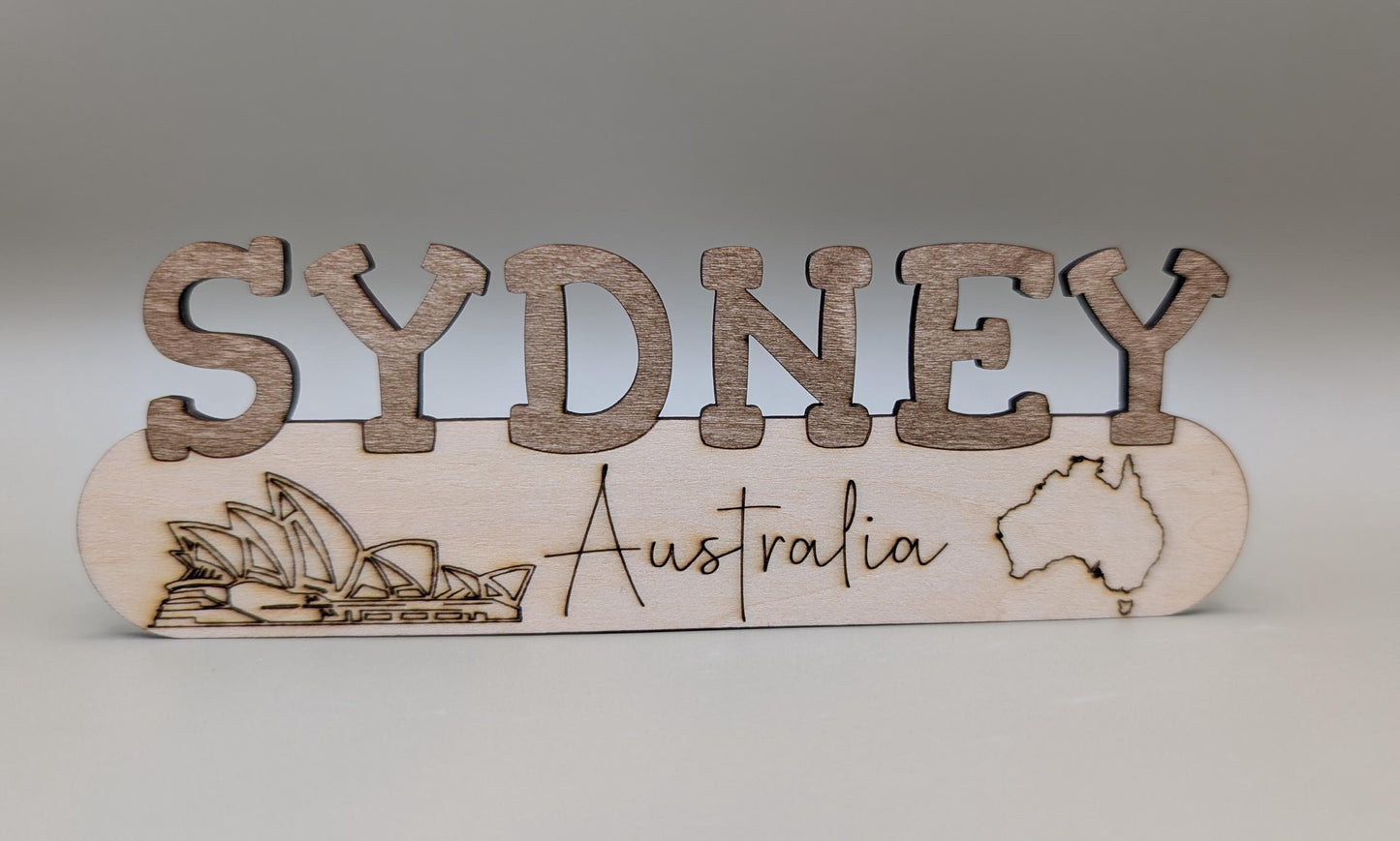 Wooden sign with 'Sydney, Australia' text and Sydney Harbour Bridge illustration on a gray background