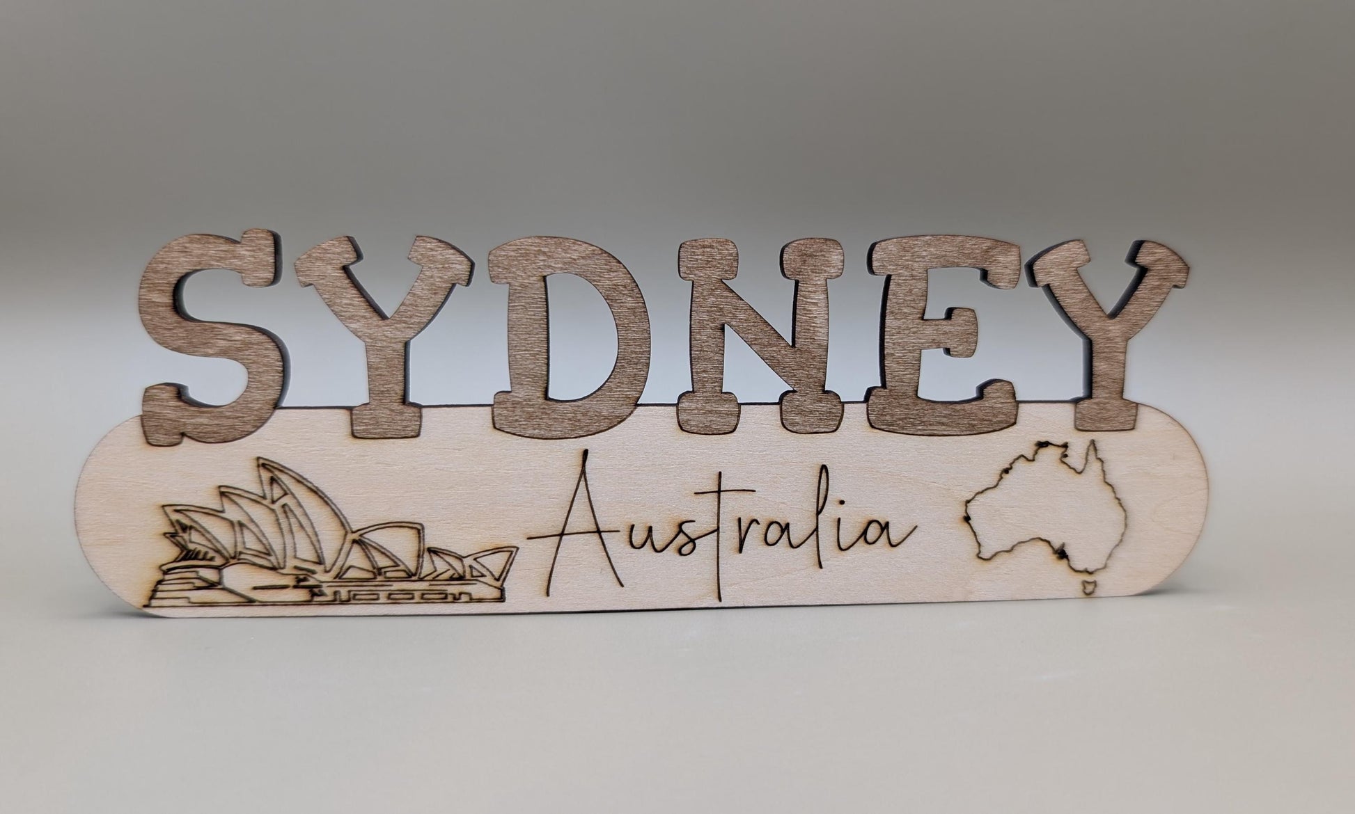 Wooden sign with 'Sydney, Australia' text and Sydney Harbour Bridge illustration on a gray background