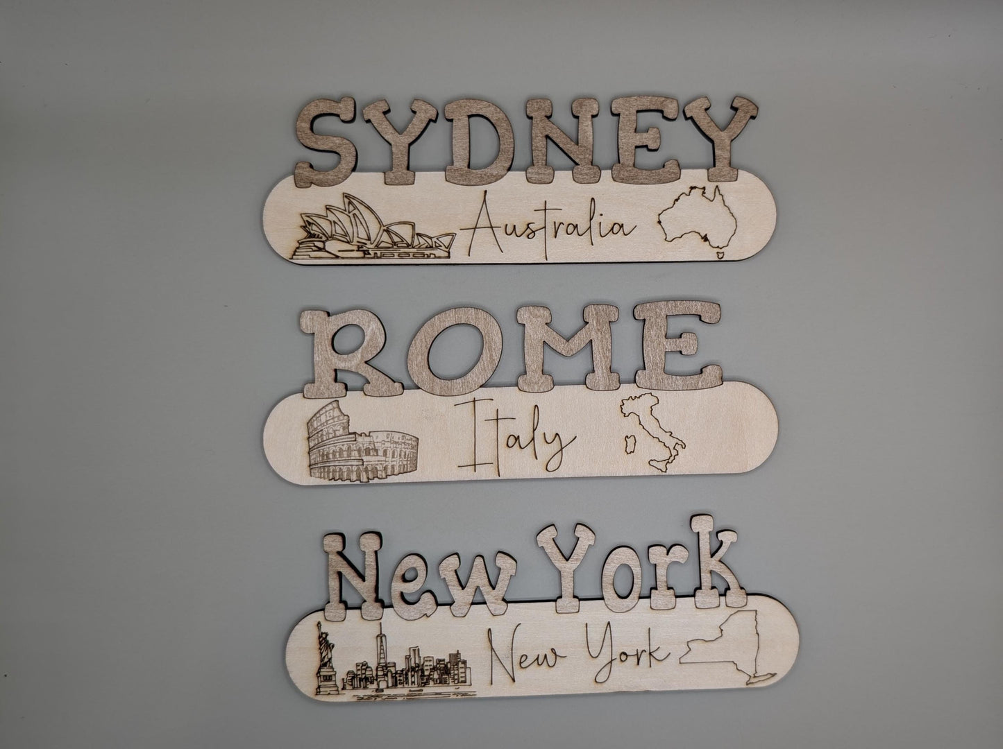 Three wooden plaques with city names and illustrations on a gray background