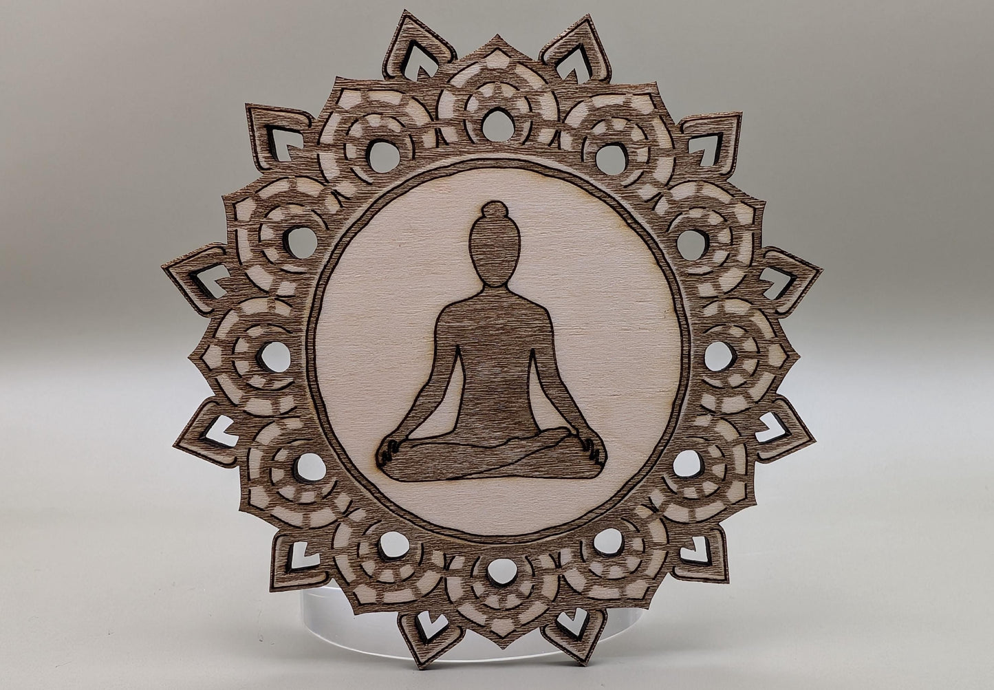 Wooden ornament with meditating figure and intricate border on a neutral background