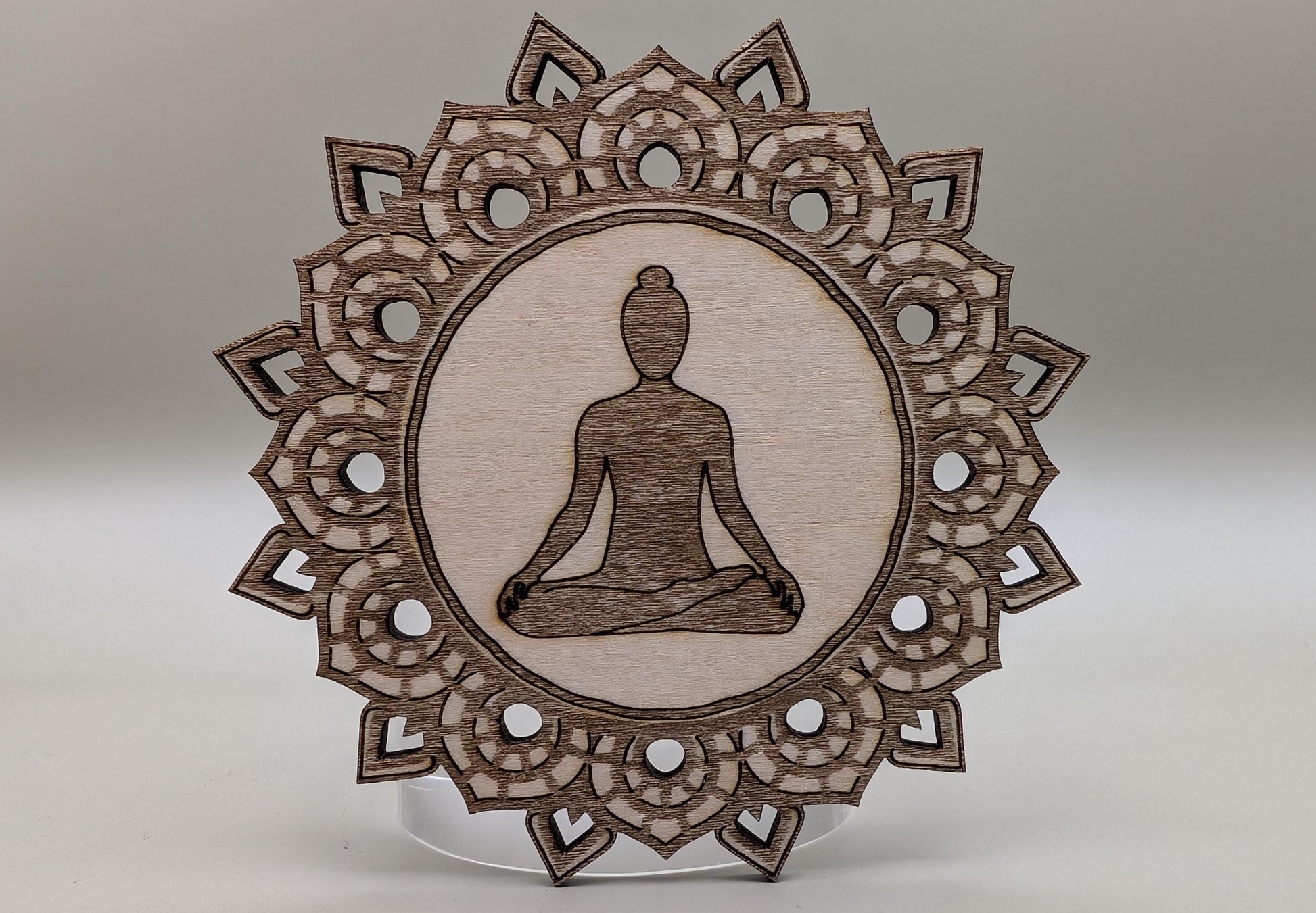 Wooden ornament with meditating figure and intricate border on a neutral background