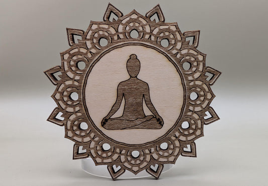 Wooden ornament with meditating figure and intricate border on a neutral background