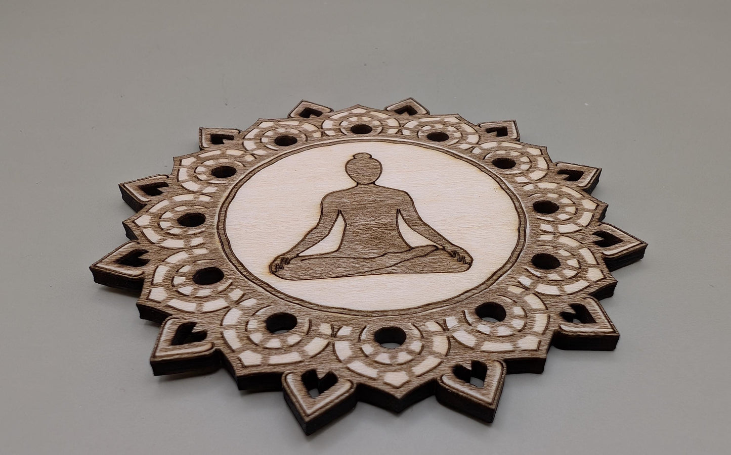 Decorative wooden coaster with a meditating figure design on a gray background