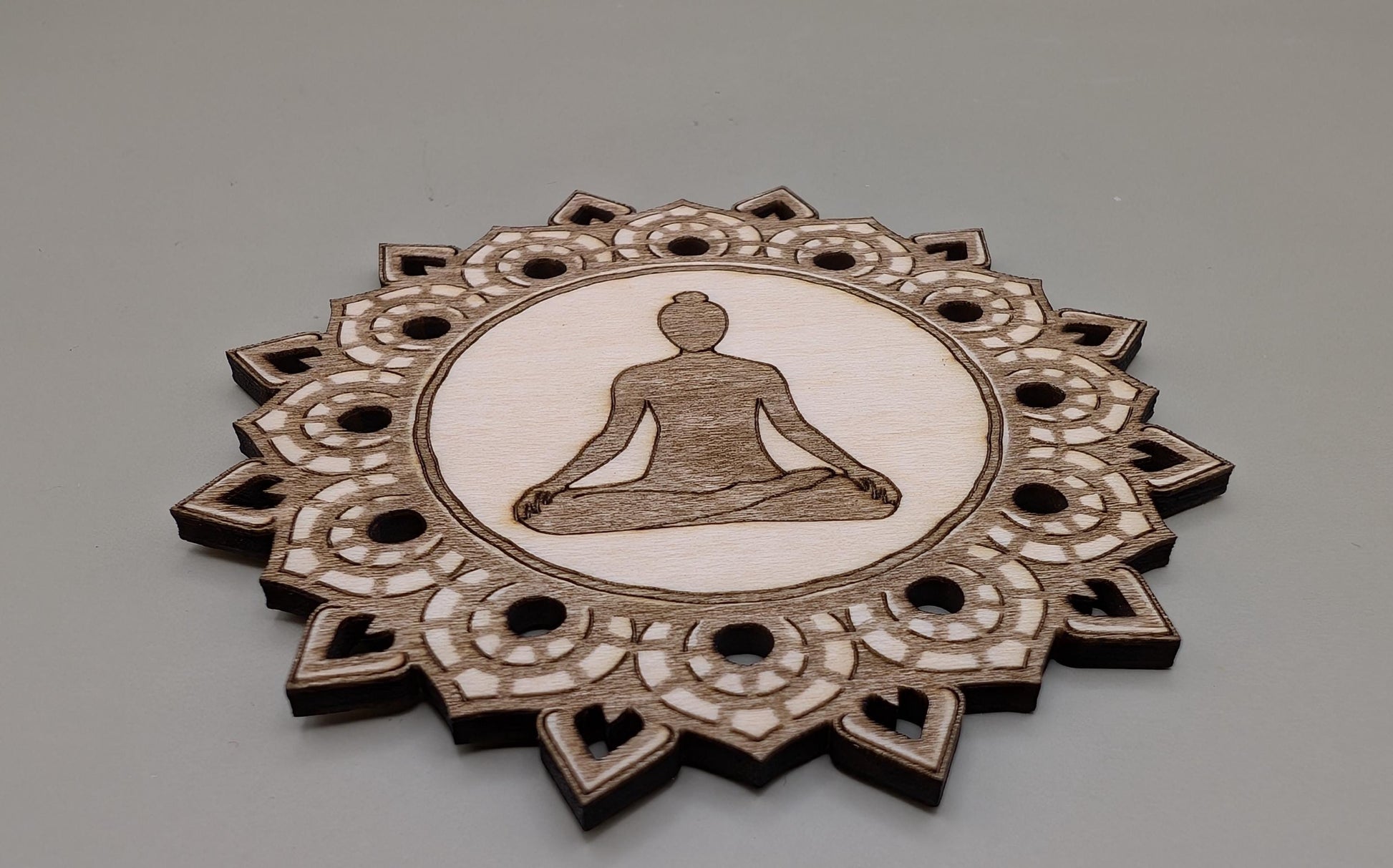 Decorative wooden coaster with a meditating figure design on a gray background