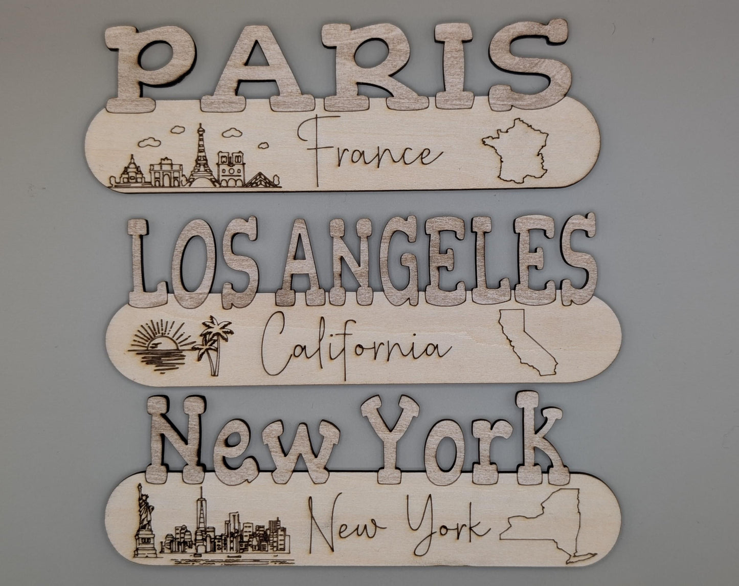 Wooden cutouts of city names with corresponding illustrations on a gray background