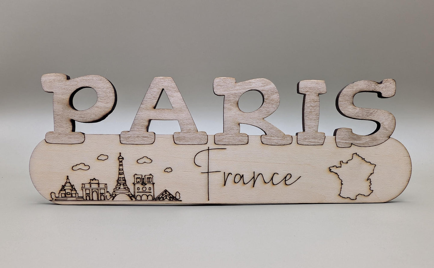 Wooden sign with 'PARIS France' and Eiffel Tower illustration on a gray background