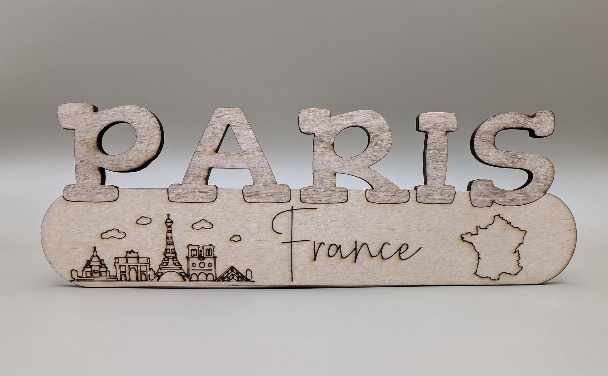 Wooden sign with 'PARIS France' and Eiffel Tower illustration on a gray background