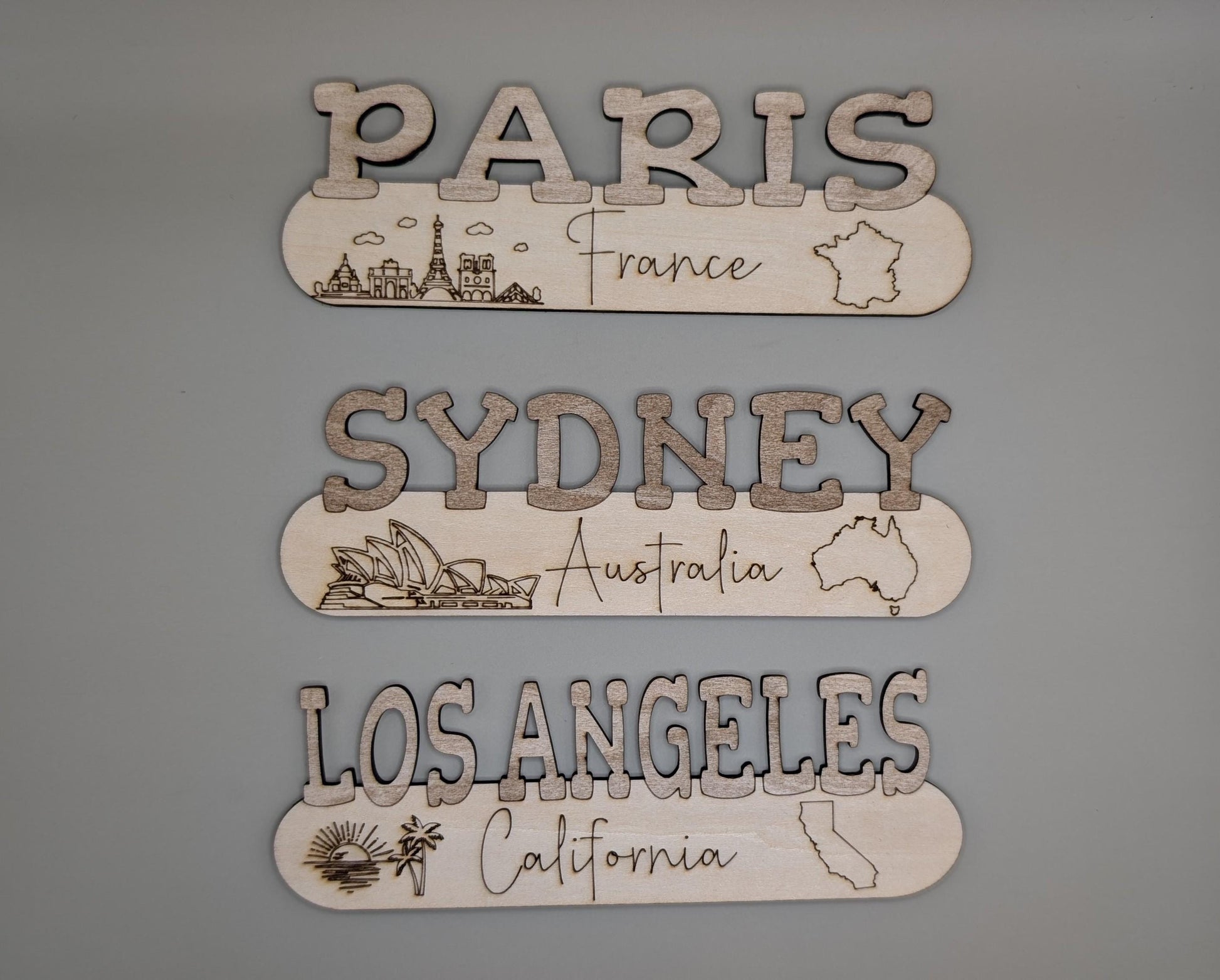 Wooden signs with 'Paris', 'Sydney', and 'Los Angeles' on a gray background