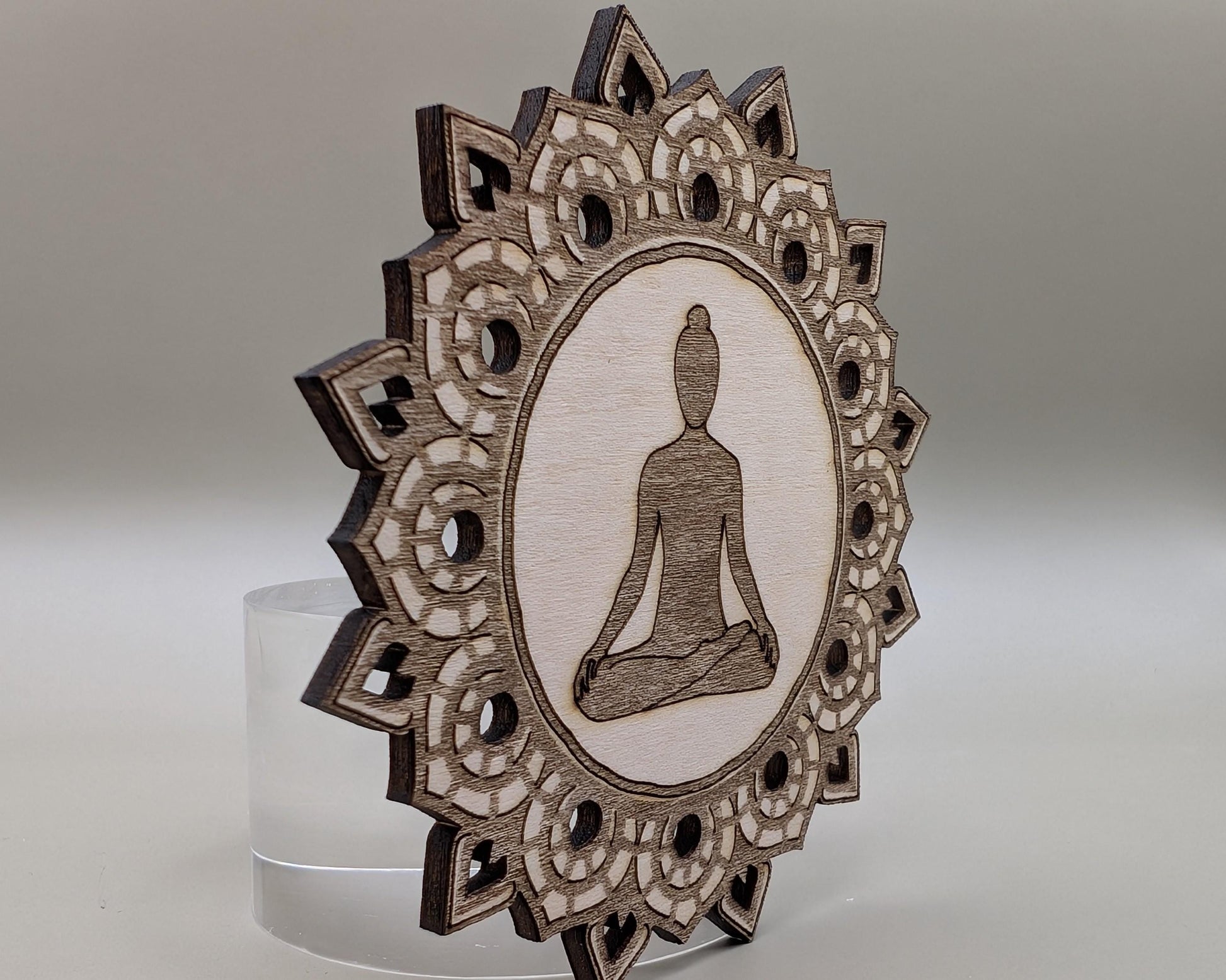 Decorative wooden ornament with a meditating figure and intricate patterns on a gray background