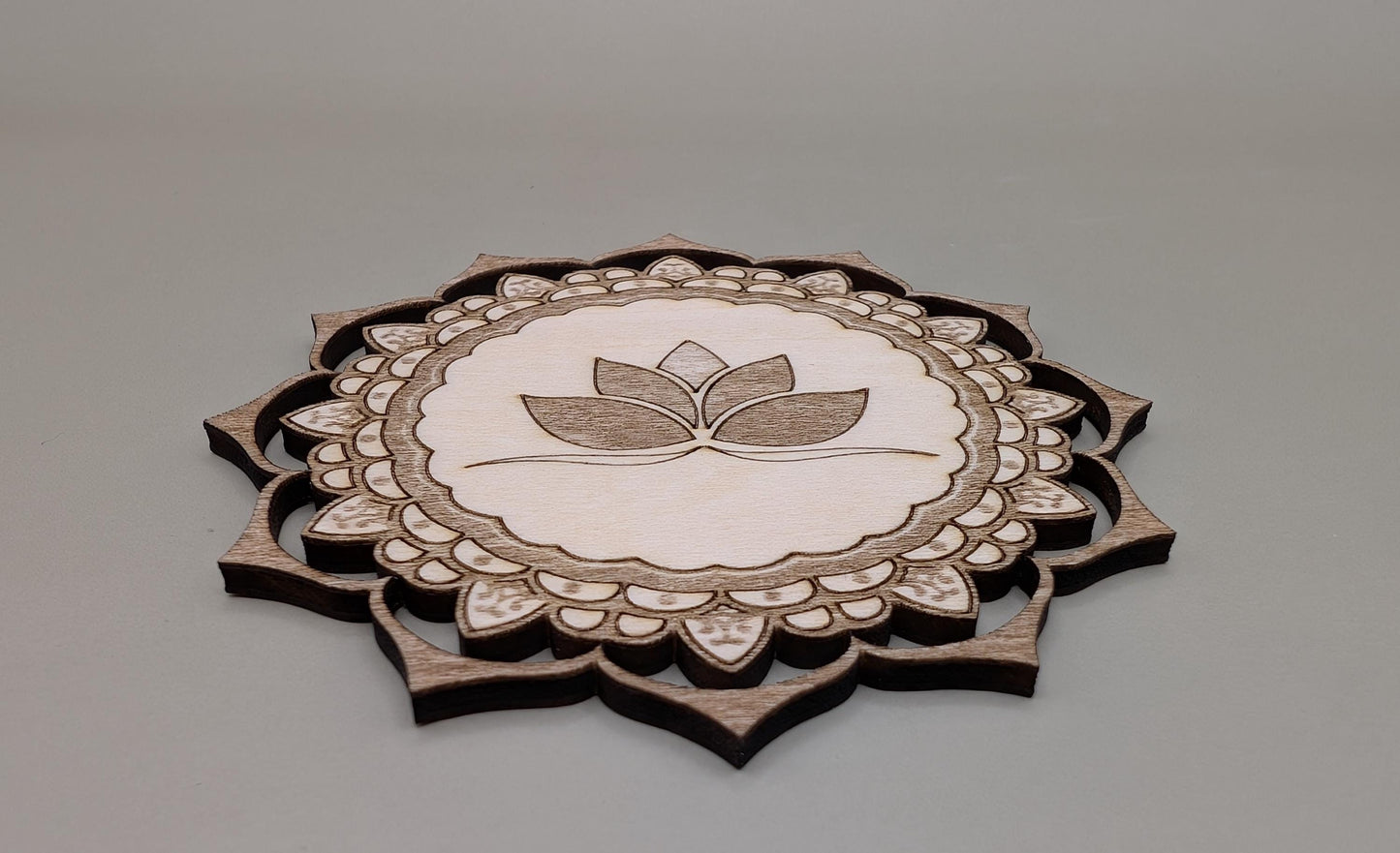 Decorative wooden coaster with lotus design on a gray background