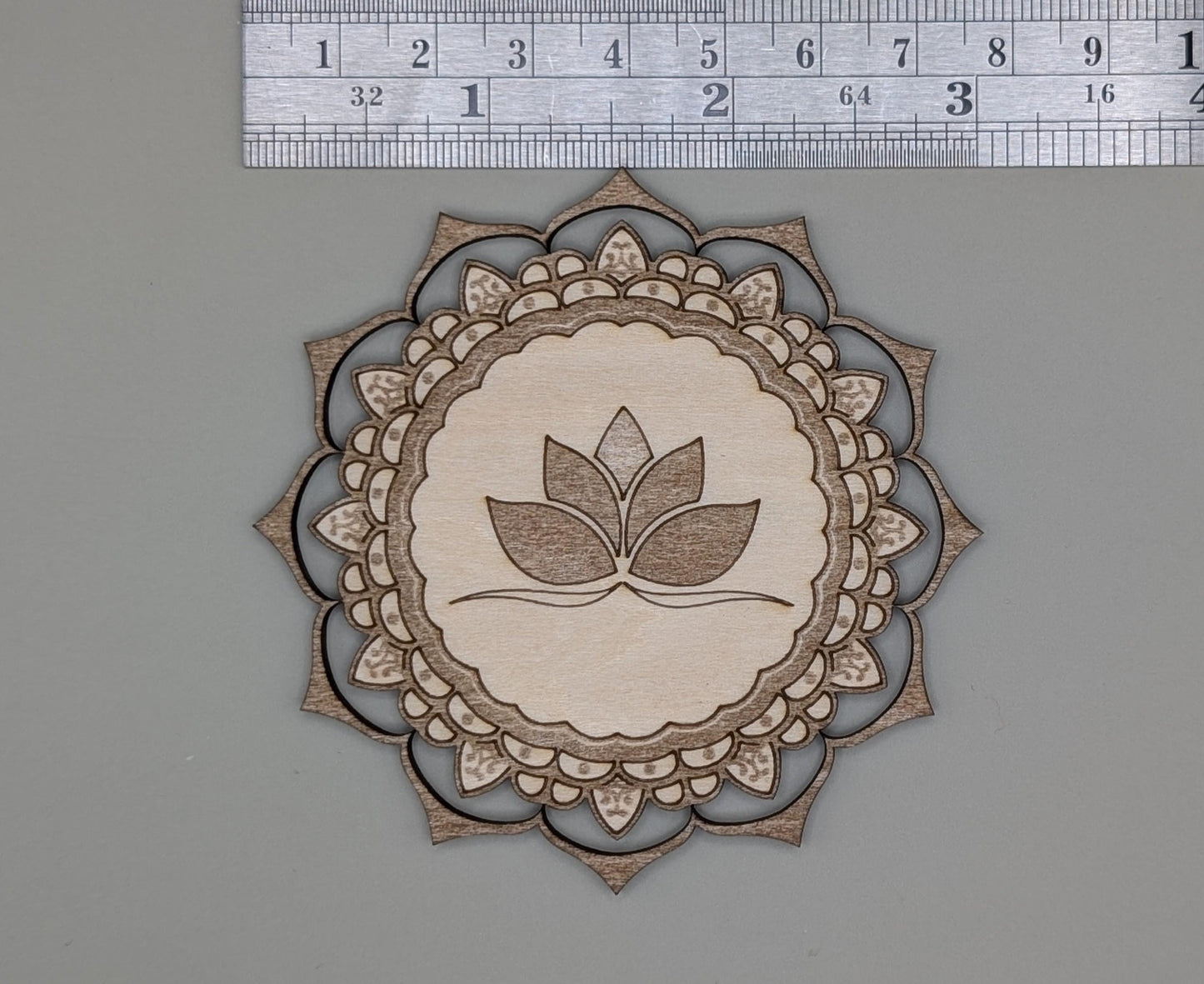 Decorative cutout with leaf design and mandala pattern on a gray background, measured against a ruler.